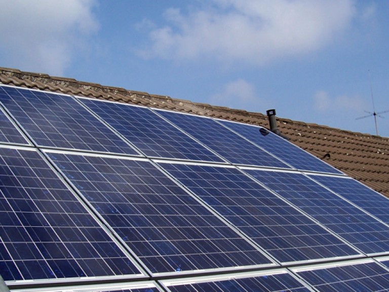 Blaue Solarmodule auf einem Dach vor blauem Himmel
